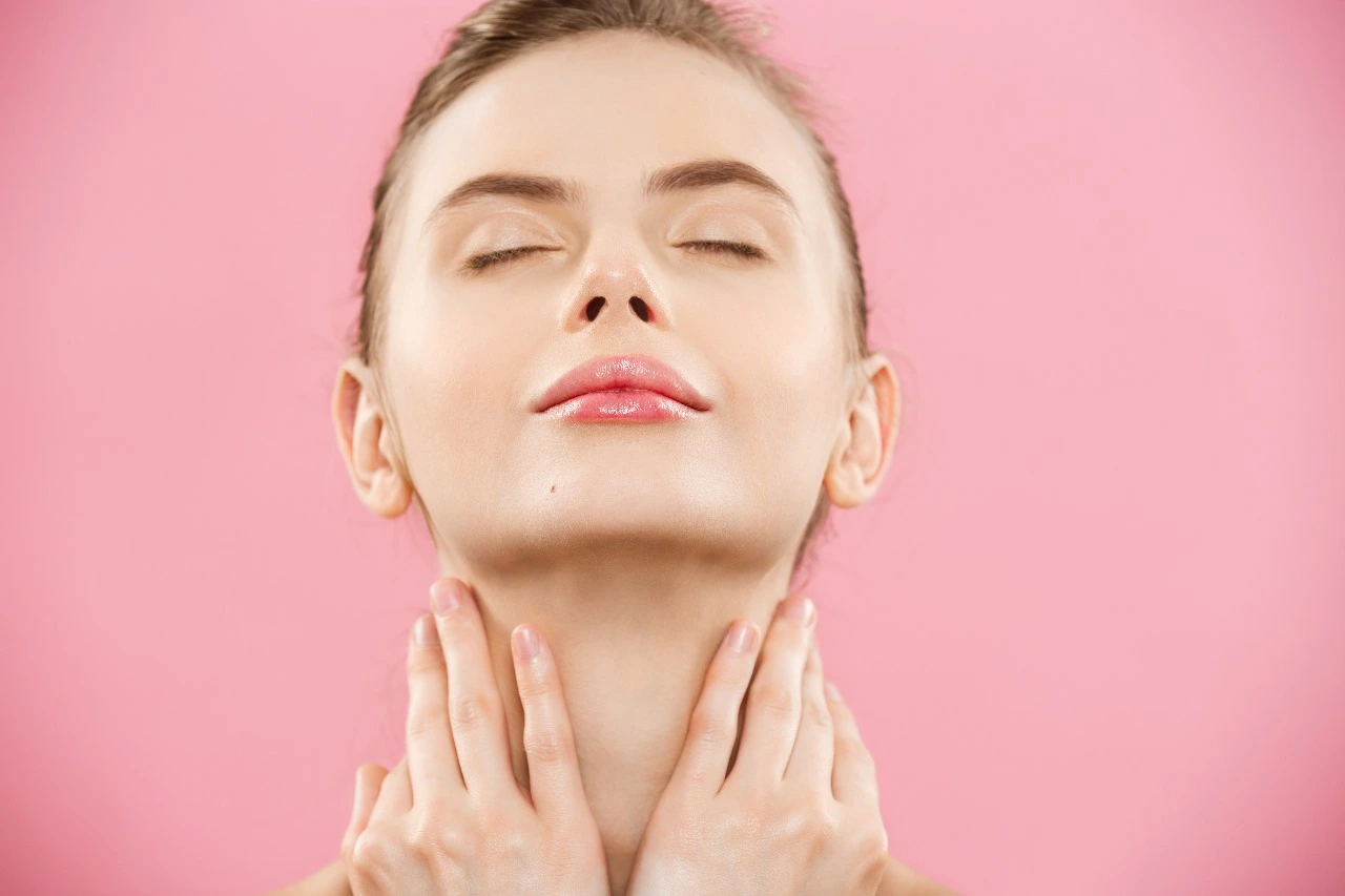 Woman with eyes closed touching her neck and jawline against pink background